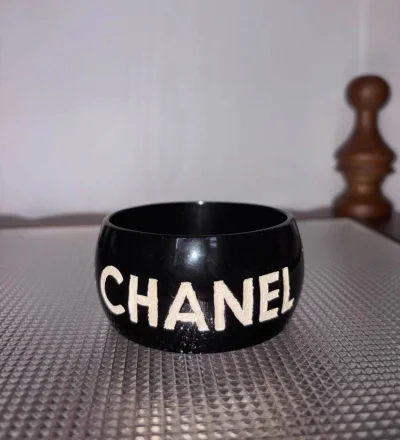 在挖煤姬刷到这只香奈儿中古镯子时，心跳漏了一拍。琉璃材质在商品图里泛着温润的光，经典菱格纹的每一道曲线都写着九十年代的优雅。
等待国际包裹的二十多天里，总担心会不会有划痕。直到拆开层层气泡纸，实物在掌心里沉甸甸的——黑金配色比想象中更典雅，岁月在镀金表面留下细密年轮...