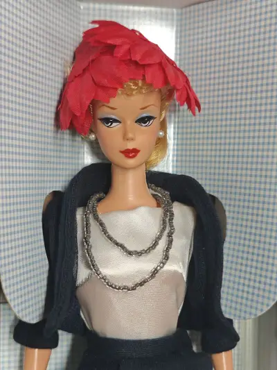 这是1998年美泰推出的**“通勤套装芭比”（Commuter Set Barbie）**，属于“收藏家请求”系列的限量复刻款，还原了1959年首款芭比的经典造型与服饰。
 
作为该系列的第二款作品，它精准复刻了1959年原版“通勤套装”（#916）的风格：深蓝色针...