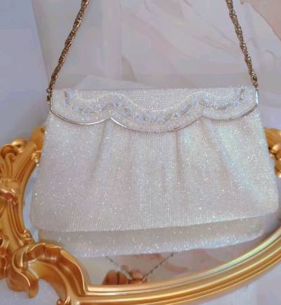 这只包包以细腻串珠手工精心编织
仿佛打翻了糖霜罐子，一颗颗晶莹剔透
扇贝形包盖设计，别致精巧
包盖上几排白色系珠子波浪设计
形状和颜色都不同
所以呈现出不同的光泽
炫彩珠会闪着蓝色的光
即使是纯白的包包，也很绚丽，设计很绝
正面采用的珠子是不规则的珠，所以很璀璨，似...