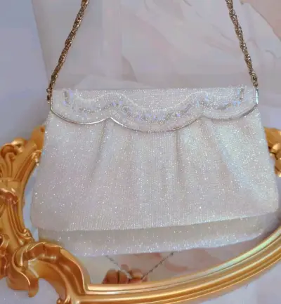 这只包包以细腻串珠手工精心编织
仿佛打翻了糖霜罐子，一颗颗晶莹剔透
扇贝形包盖设计，别致精巧
包盖上几排白色系珠子波浪设计
形状和颜色都不同
所以呈现出不同的光泽
炫彩珠会闪着蓝色的光
即使是纯白的包包，也很绚丽，设计很绝
正面采用的珠子是不规则的珠，所以很璀璨，似...