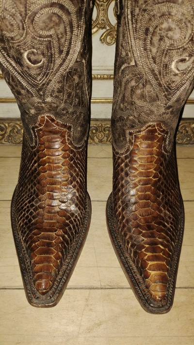 这双蟒蛇皮西部靴堪称复古与个性的完美融合，极具辨识度的蟒纹肌理自带野性张力，做旧的棕调渐变让鳞片纹理在光线下呈现出丰富的层次变化，搭配靴筒精致的雕花缝线，既有美式西部的粗粝硬朗，又暗藏哥特式的华丽质感。
 
鞋型利落的尖靴头与低方跟设计兼顾了视觉冲击力与穿着舒适度，...