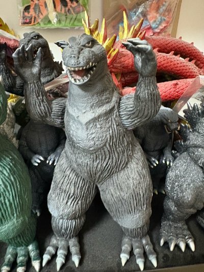 这是1962版金刚大战哥斯拉造型的哥斯拉软胶，属于经典复古款。
通体灰黑配色，皮肤布满纵向纹理，双臂抬起的姿态还原了影片中与金刚对峙的经典场景，肌肉线条与爪部细节刻画扎实，是哥斯拉系列早期形象的代表性周边，收藏与怀旧价值突出。
