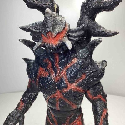 这款怪兽软胶通体焦黑底色搭配烈焰般的红纹涂装，造型极具压迫感。头部尖锐突起与獠牙狰狞恐怖，身体布满粗糙的岩石质感纹理，背后巨大的棘刺结构霸气十足，整体尽显黑暗系怪兽的狂暴与诡异，是特摄收藏中风格强烈的一款。