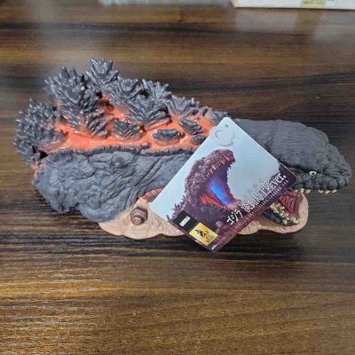 这款新哥斯拉（淡路岛上陆ver.）软胶，以匍匐姿态还原剧中登场场景。灰黑表皮褶皱粗糙，背鳍橙红熔岩纹路极具张力，地台与螺栓细节还原战场氛围，是充满叙事感的收藏款。