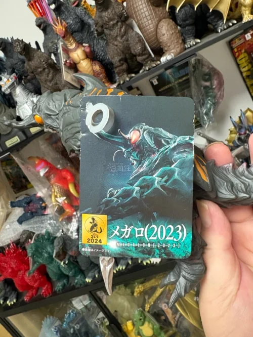 这款万代2023美加洛软胶造型还原电影形象，灰紫主体搭配橙纹质感出色，巨爪、头角细节雕刻细腻，软胶材质手感柔和，挂卡完整收藏价值高，是哥斯拉怪兽系列优质单品。