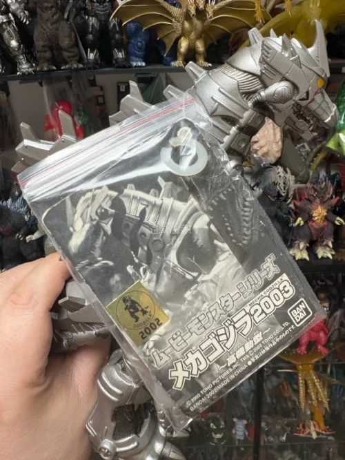这款万代2003三式机龙软胶质感扎实，金属银涂装机械细节拉满，尾棘、管线刻画精致。原配吊牌完整，背景哥斯拉藏品柜氛围感十足，老胶收藏价值很高。