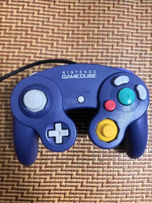 这是一台任天堂GameCube（NGC）家用游戏机，经典的紫罗兰紫配色。
机身上方是光盘仓，正面配备四个手柄接口，下方有SLOT‑A、SLOT‑B两个记忆卡插槽，右下角印有ATI的标识，代表该机的图形芯片由ATI提供。
 这台是任天堂2001年推出的第六代家用主机，...