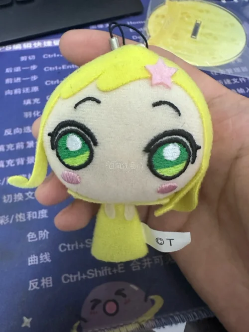 小魔女Doremi妖精挂件。采用毛绒布料和刺绣工艺制成，整体为黄色，复刻了角色标志性的金色双马尾、绿色大眼睛和头顶的粉色星星发夹
