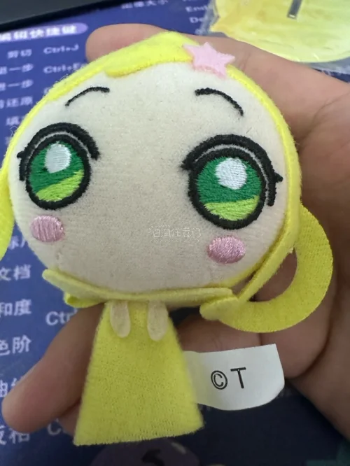 小魔女Doremi妖精挂件。采用毛绒布料和刺绣工艺制成，整体为黄色，复刻了角色标志性的金色双马尾、绿色大眼睛和头顶的粉色星星发夹
